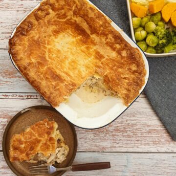An overhead shot of granny's chicken pie with a slice removed and served on a plate next to the baking dish.