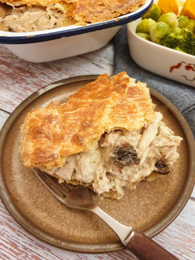 A slice of chicken pie on a plate with the filling spilling out.