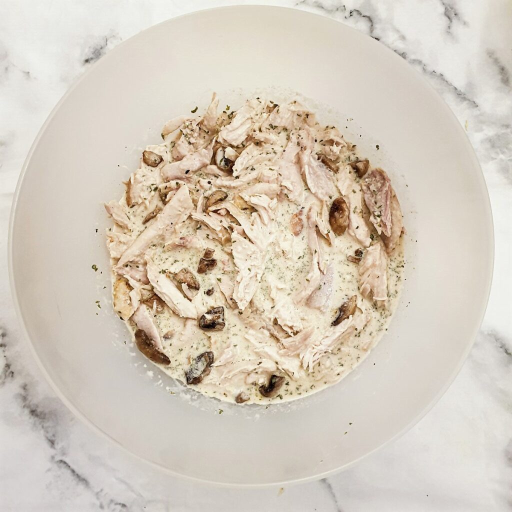 A mixing bowl with a mixture of shredded chicken, fried mushrooms and milk and soup mixture.