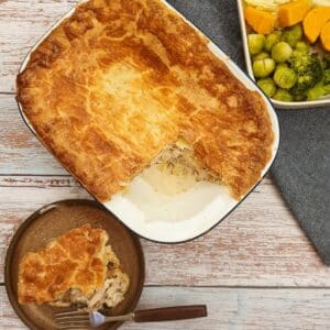 An overhead shot of granny's chicken pie with a slice removed and served on a plate next to the baking dish.
