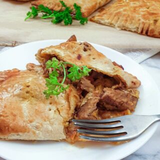 A lamb pie on a plate, cut open to show the meat inside.