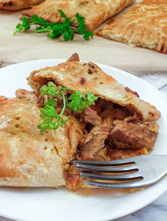 A lamb pie on a plate, cut open to show the meat inside.