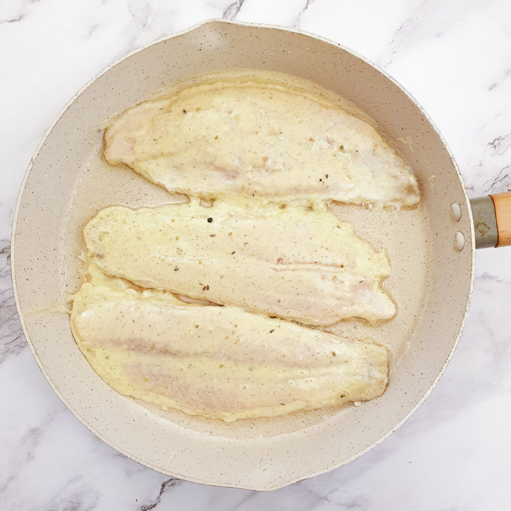 Three fillets of fish being fried in a frying pan.