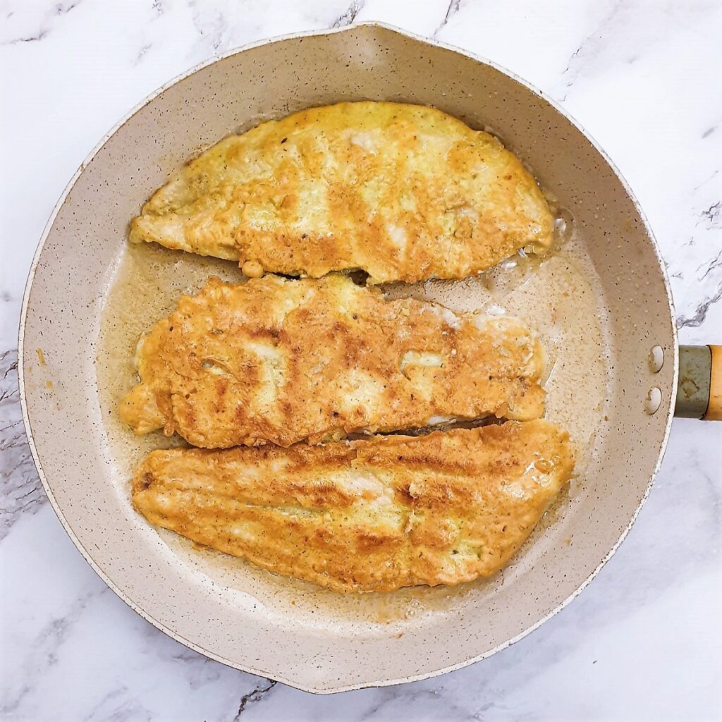 Three fillets of fish in a frying pan showing the golden brown batter.