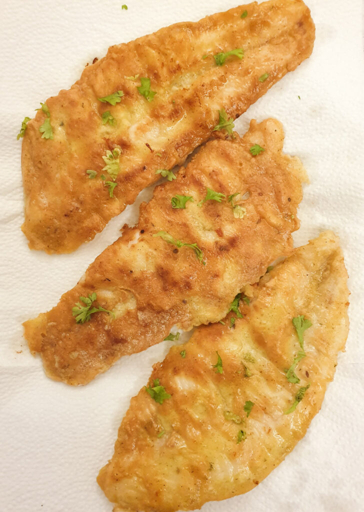 Three pan-fried fish fillets draining on paper towel.