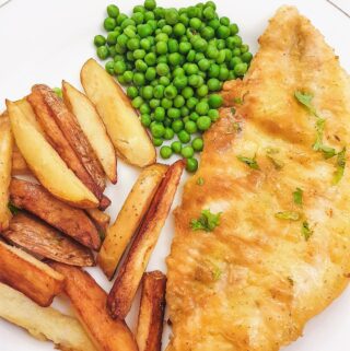 A golden pan-fried fish fillet on a plate with chips and peas.