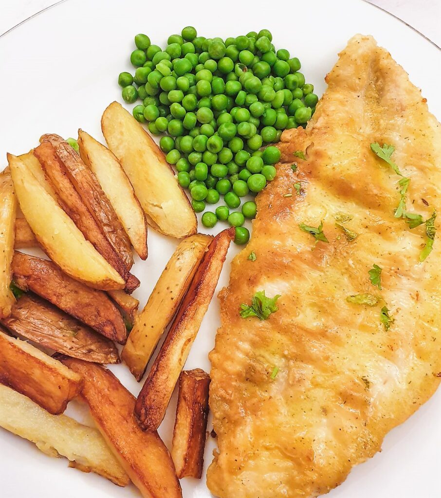 A golden pan-fried fish fillet on a plate with chips and peas.