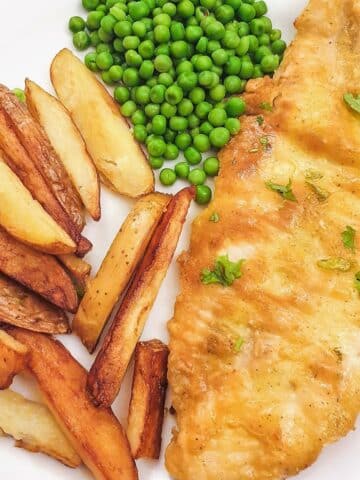 A golden pan-fried fish fillet on a plate with chips and peas.