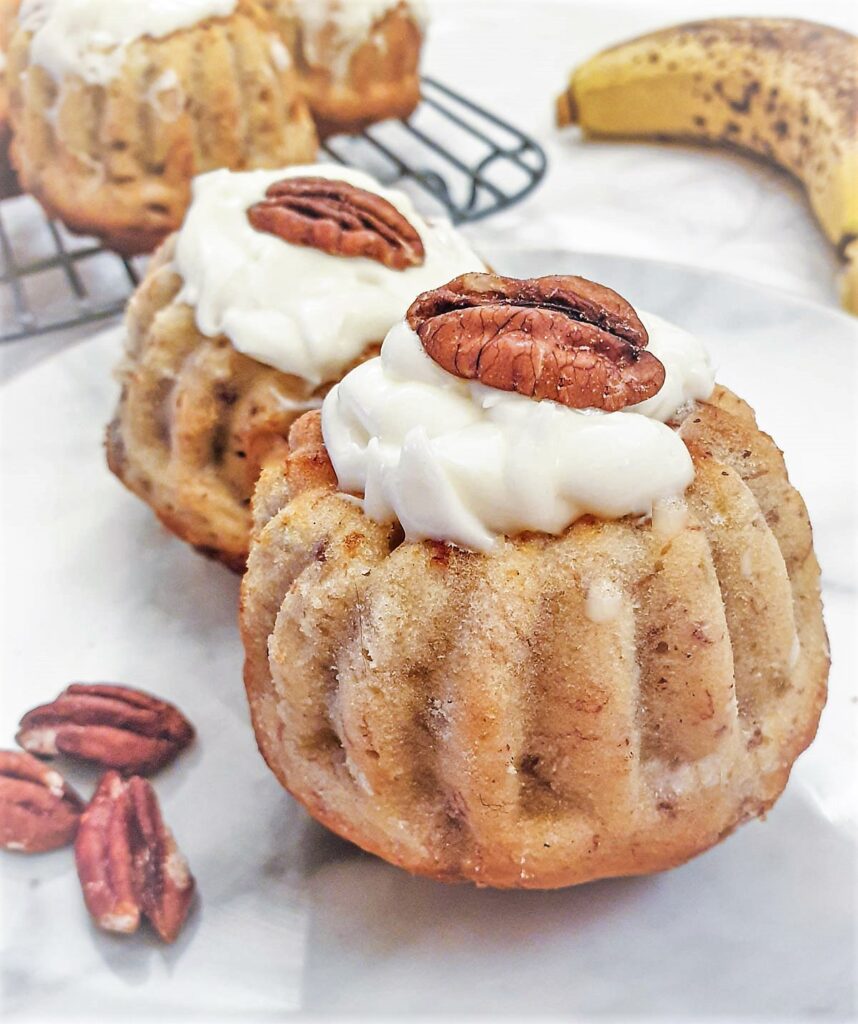 Close up of a pecan and banana bundt cake filled with lemon cheese frosting and topped with a pecan nut.