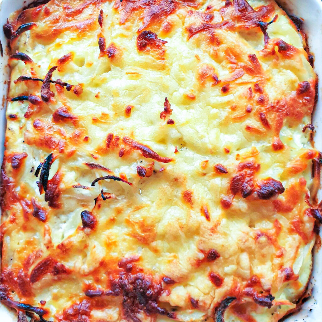 A dish of baked potato and onion with cheesy topping.