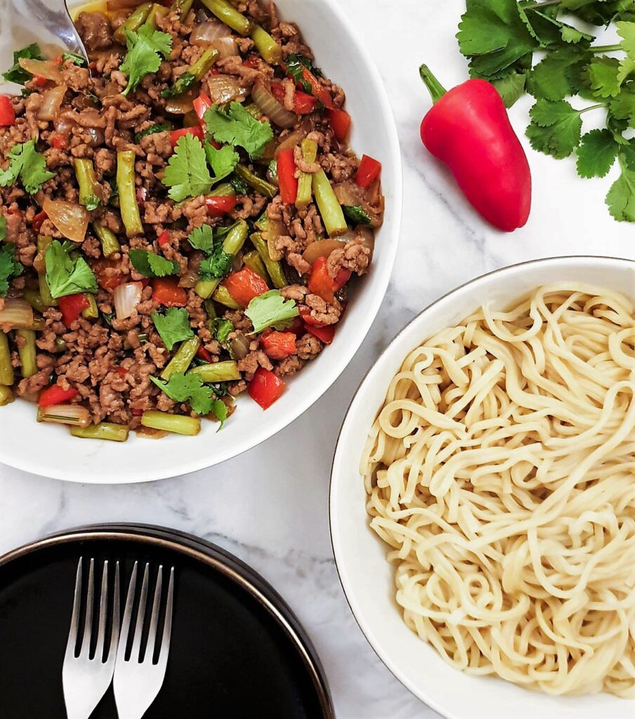 Overhead shot of a dish of Thai pork mince stir fry with a dish of noodles. Overhead shot of a dish of Thai pork mince stir fry with a dish of noodles.