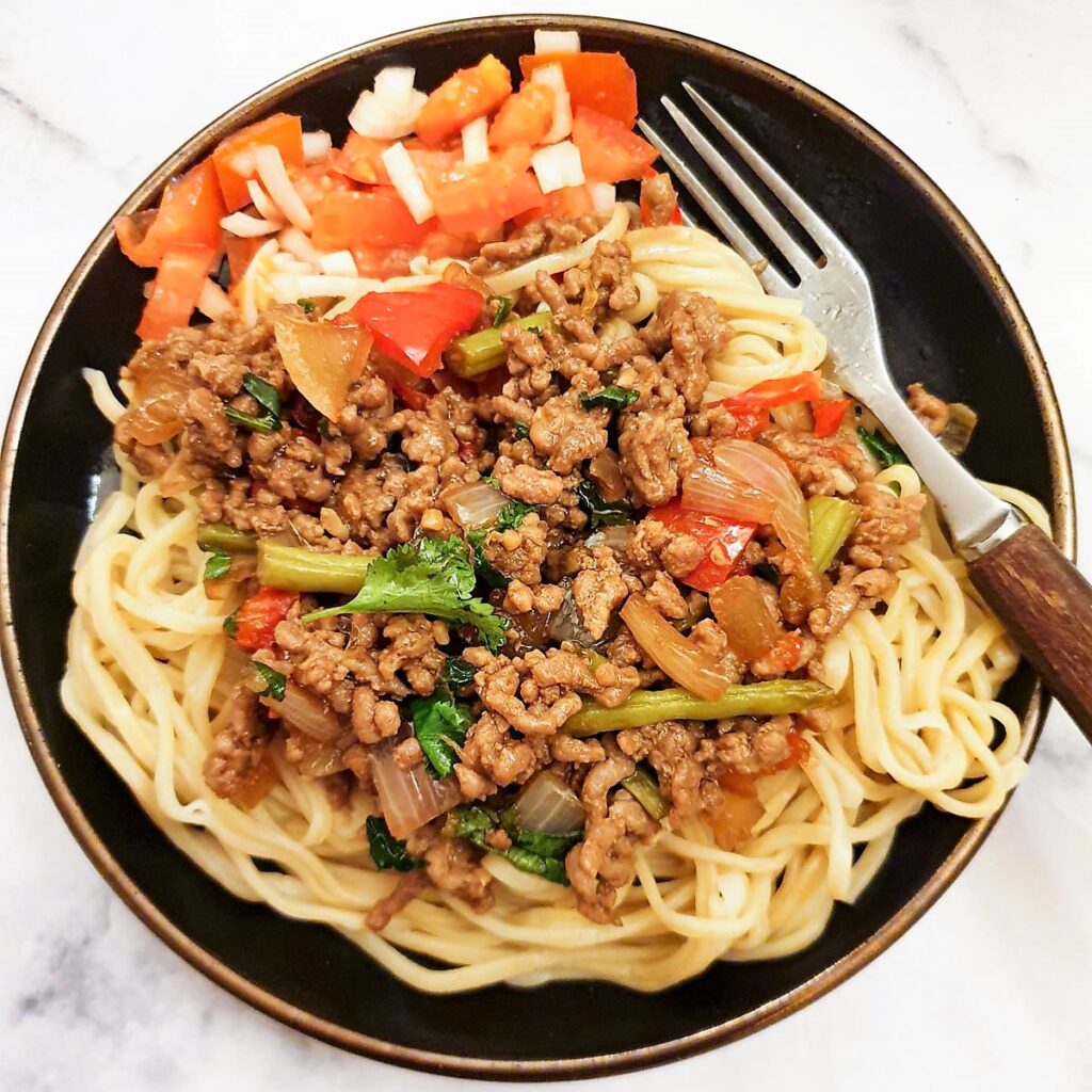 Close up of a plate of Thai pork mince stir fry with a side helping of chopped tomatoes and onions.