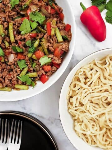 Overhead shot of a dish of Thai pork mince stir fry with a dish of noodles.