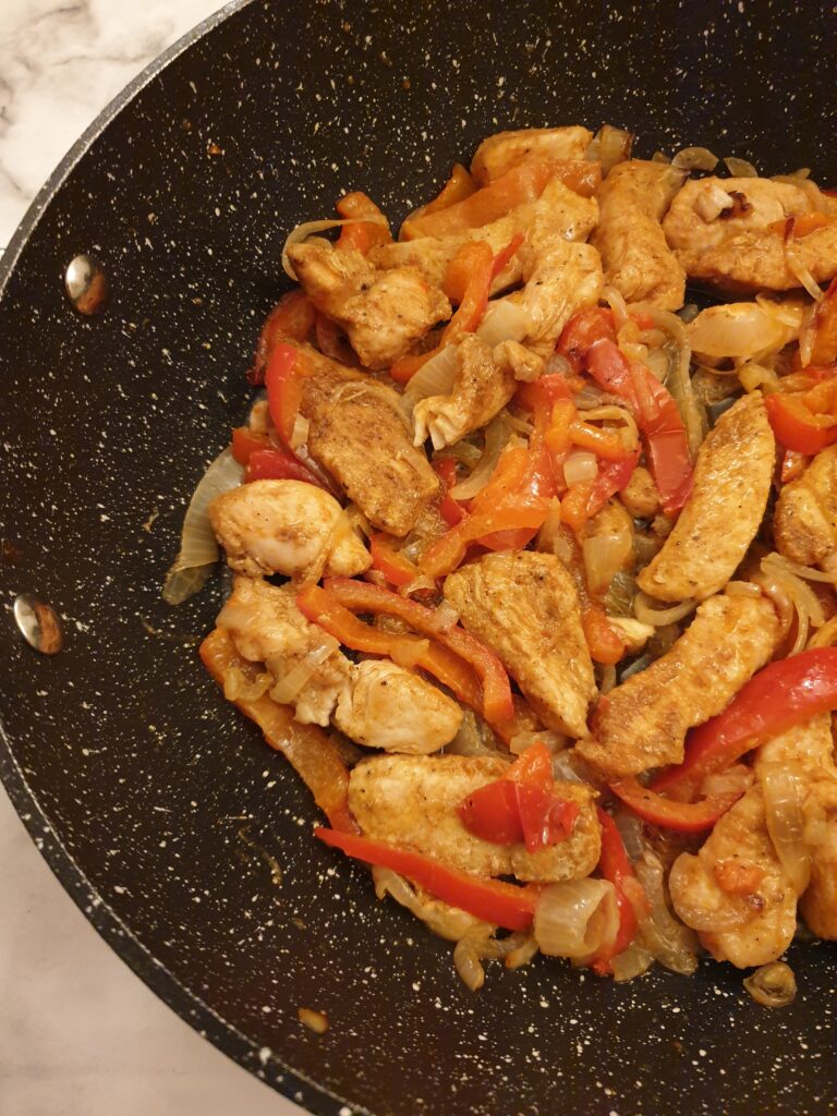 Chicken strips in a pan with onions and capsicums.