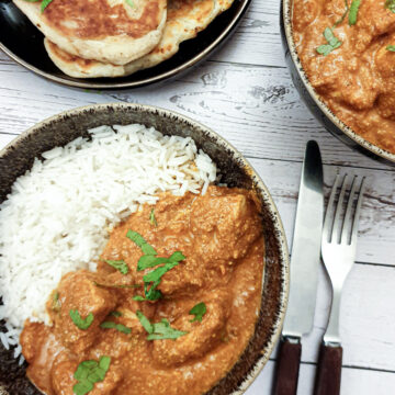 Chicken tikka masla in a bowl with rice next to a plate of naan bread.