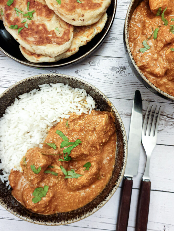 Chicken tikka masla in a bowl with rice next to a plate of naan bread.