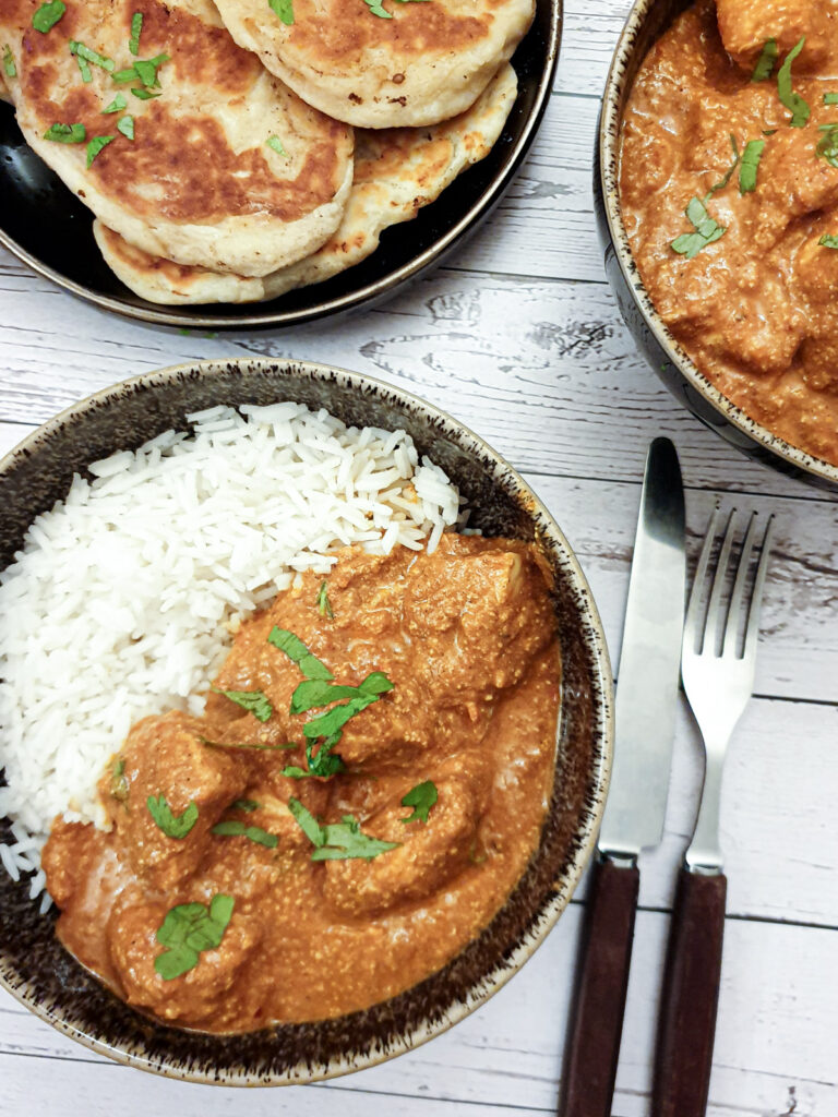 Chicken tikka masla in a bowl with rice next to a plate of naan bread. Chicken tikka masla in a bowl with rice next to a plate of naan bread.