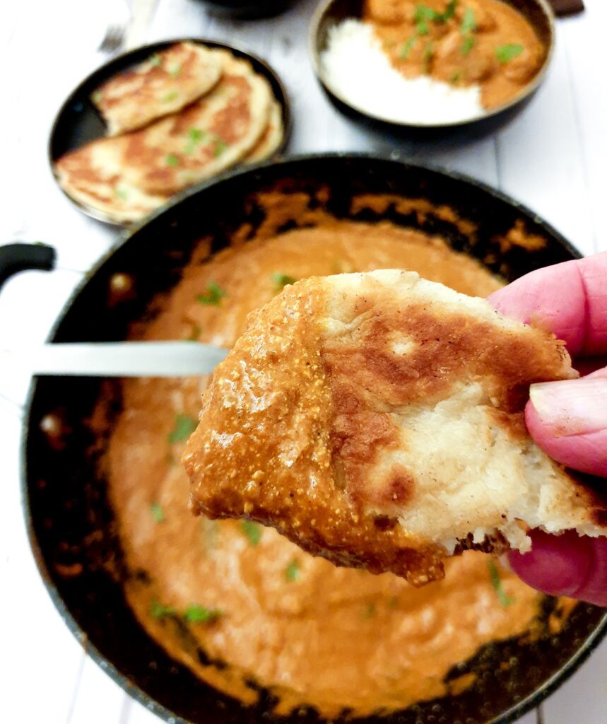 A piece of naan bread dipped in the chicken tikka masala sauce.