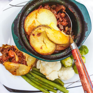 An individual serving dish filled with minced beef hotpot on a plate with vegetables.