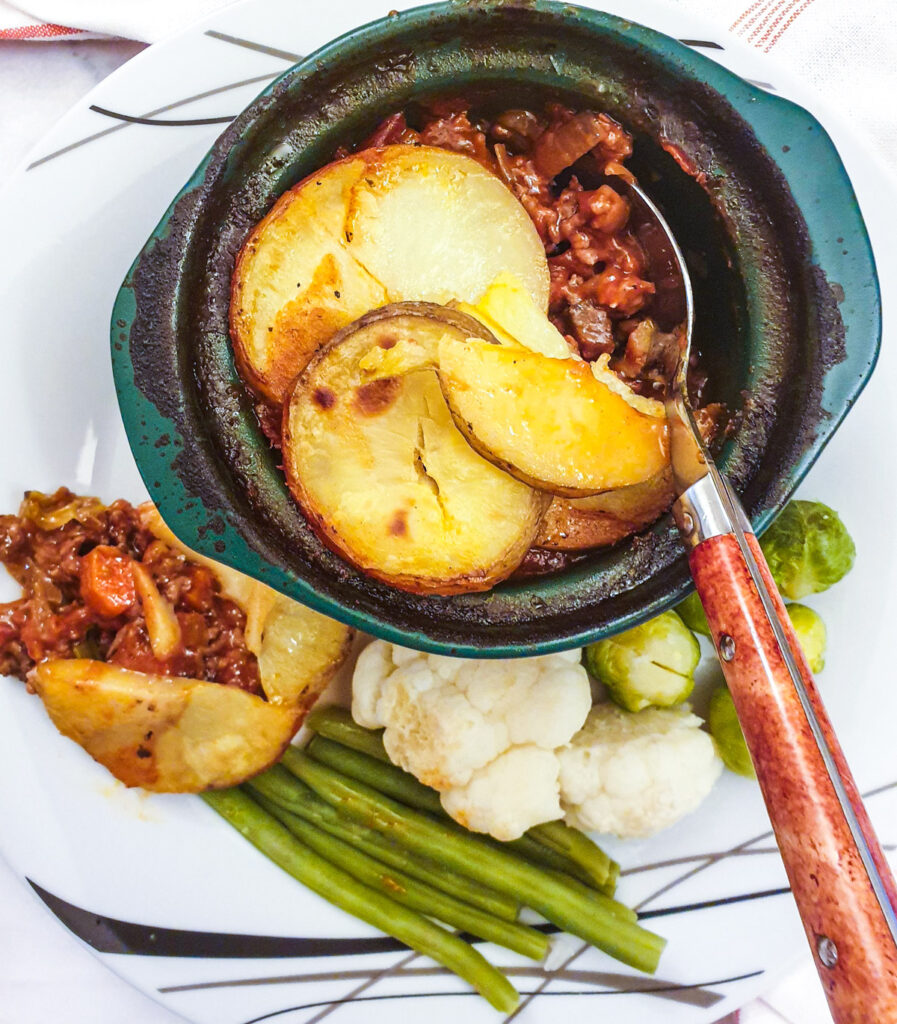 An individual serving dish filled with minced beef hotpot on a plate with vegetables.