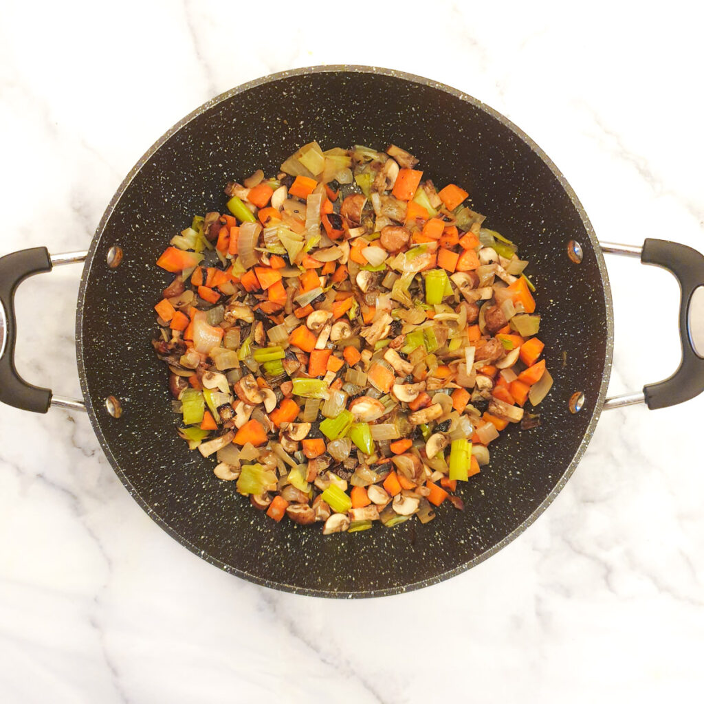 Diced vegetables cooking in a frying pan.