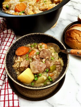 Lamb stew in a bowl next to a plate of crusty bread rolls.