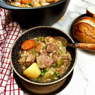 Lamb stew in a bowl next to a plate of crusty bread rolls.