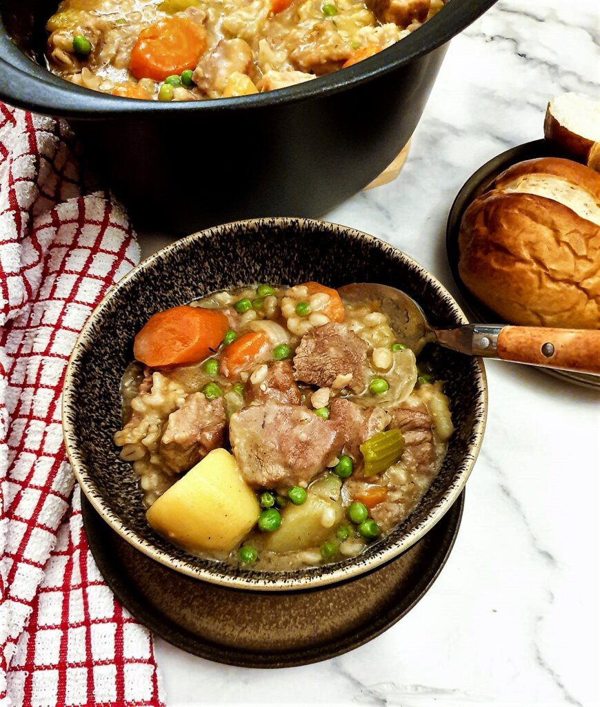 Lamb stew in a bowl next to a plate of crusty bread rolls.