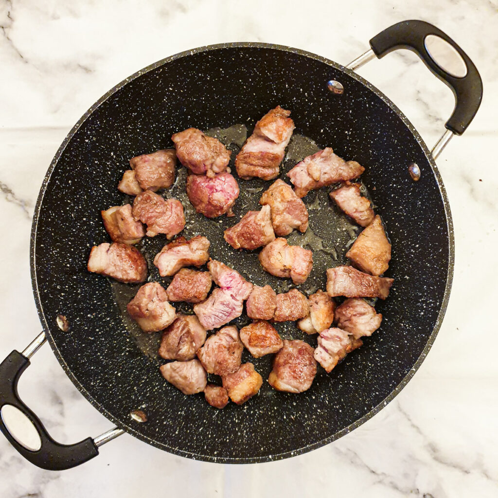 Lamb chunks browning in a frying pan.