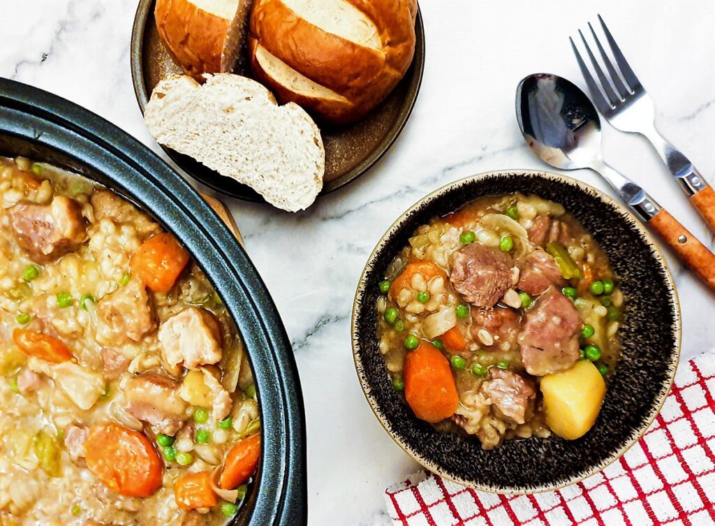 A bowl of Irish stew next to a plate of crusty bread.