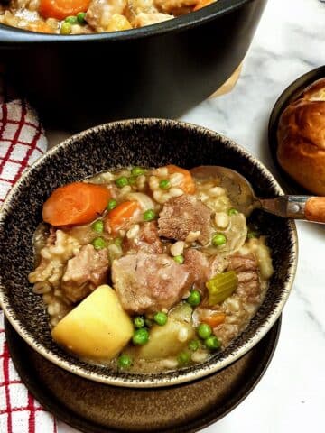 Lamb stew in a bowl next to a plate of crusty bread rolls.