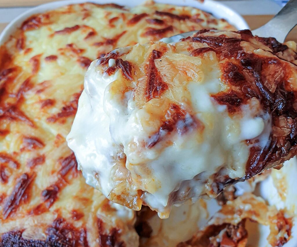 A spoonful of pancakes stuffed with meat and covered with cheese being lifted from the serving dish.