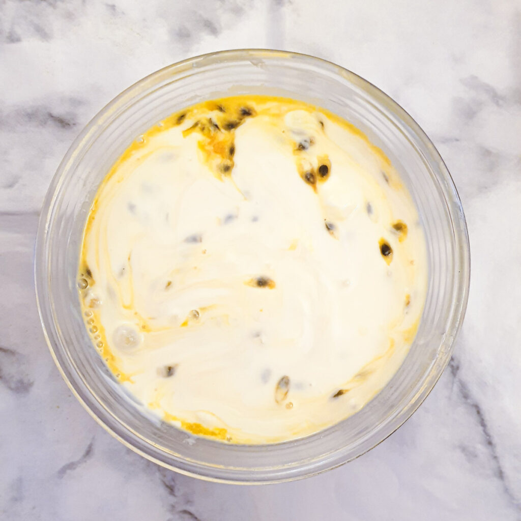 Yoghurt, condensed milk and passion fruit pulp combined in a mixing bowl.