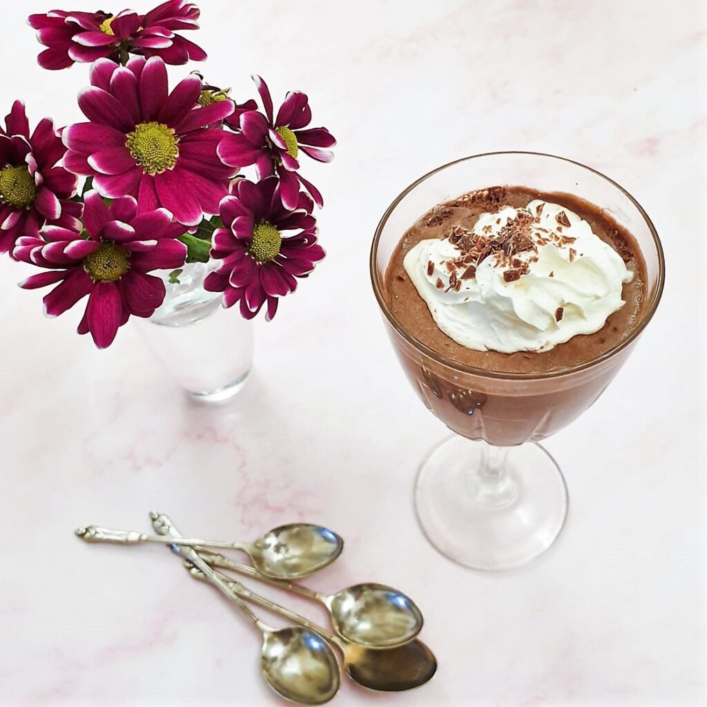 A glass of peppermint chocolate mousse, topped with whipped cream, next to a purple chrysanthemum.