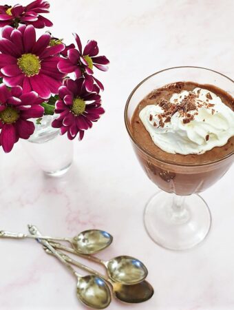 A glass of peppermint chocolate mousse, topped with whipped cream, next to a purple chrysanthemum.