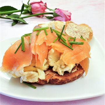 Scrambled eggs on a slice of toast, topped with sliced smoked salmon and garnished with chopped chives.