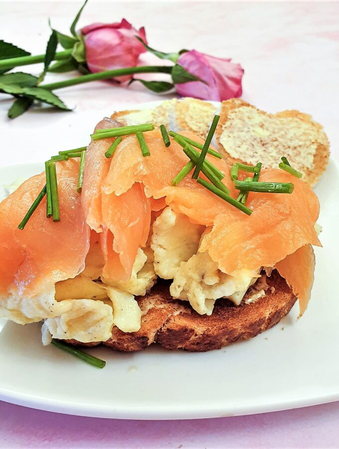 Scrambled eggs on a slice of toast, topped with sliced smoked salmon and garnished with chopped chives.