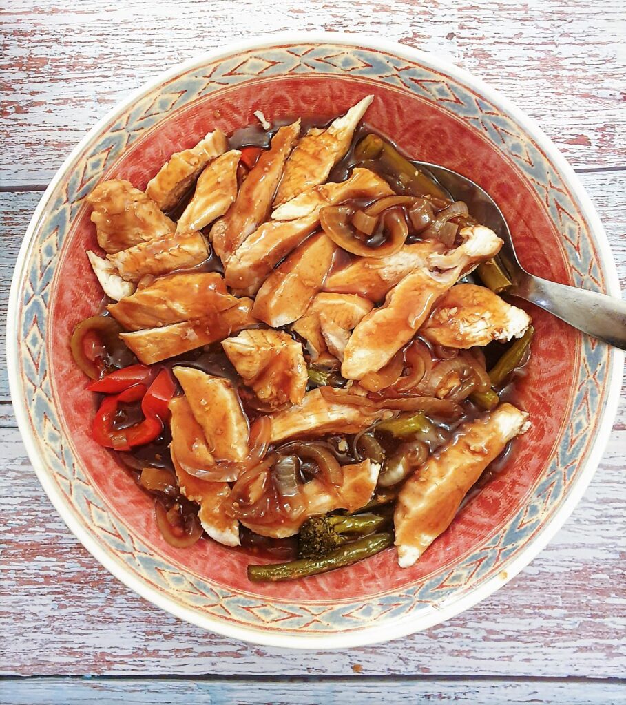 A serving dish filled with the sliced chicken on top of the vegetables, covered with teriyaki sauce.