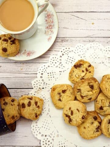 Chocolate chip and brazil nut cookies on a doily next to a cup of tea.