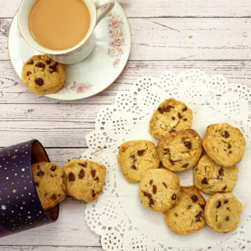 Chocolate chip and brazil nut cookies on a doily next to a cup of tea.