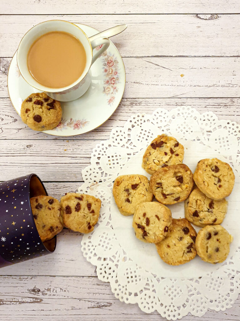 Chocolate chip and brazil nut cookies on a doily next to a cup of tea.