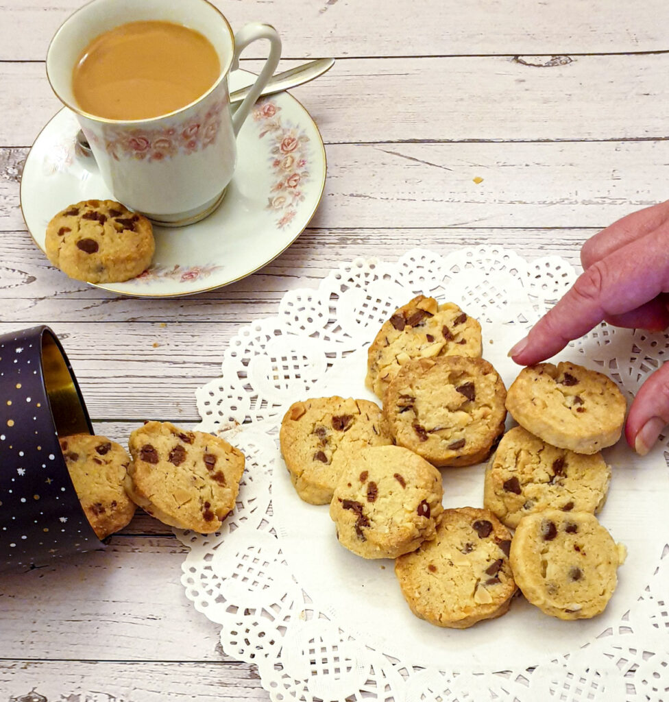 A choc-chip brazil nut cookie being lifted from a plate.