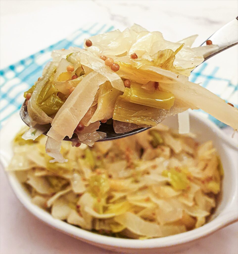 Closeup of a spoonful of cabbage and leeks with mustard seeds.