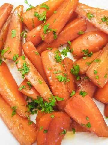 Close up of glazed carrots garnished with chopped parsley on a white plate.