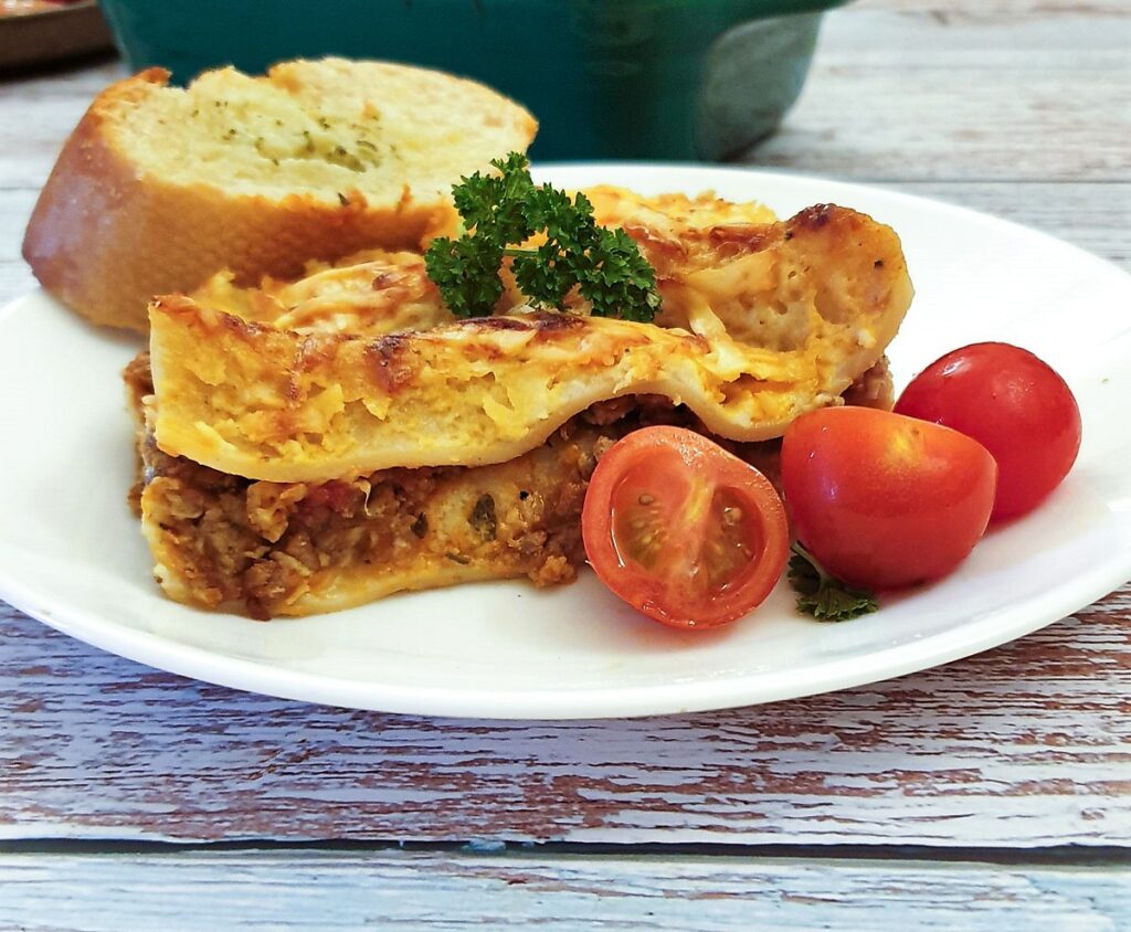 A slice of lasagne on a plate with tomatoes.