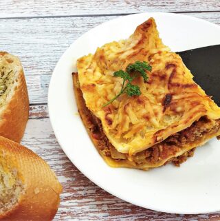 A slice of lasagne being lifted onto a plate.