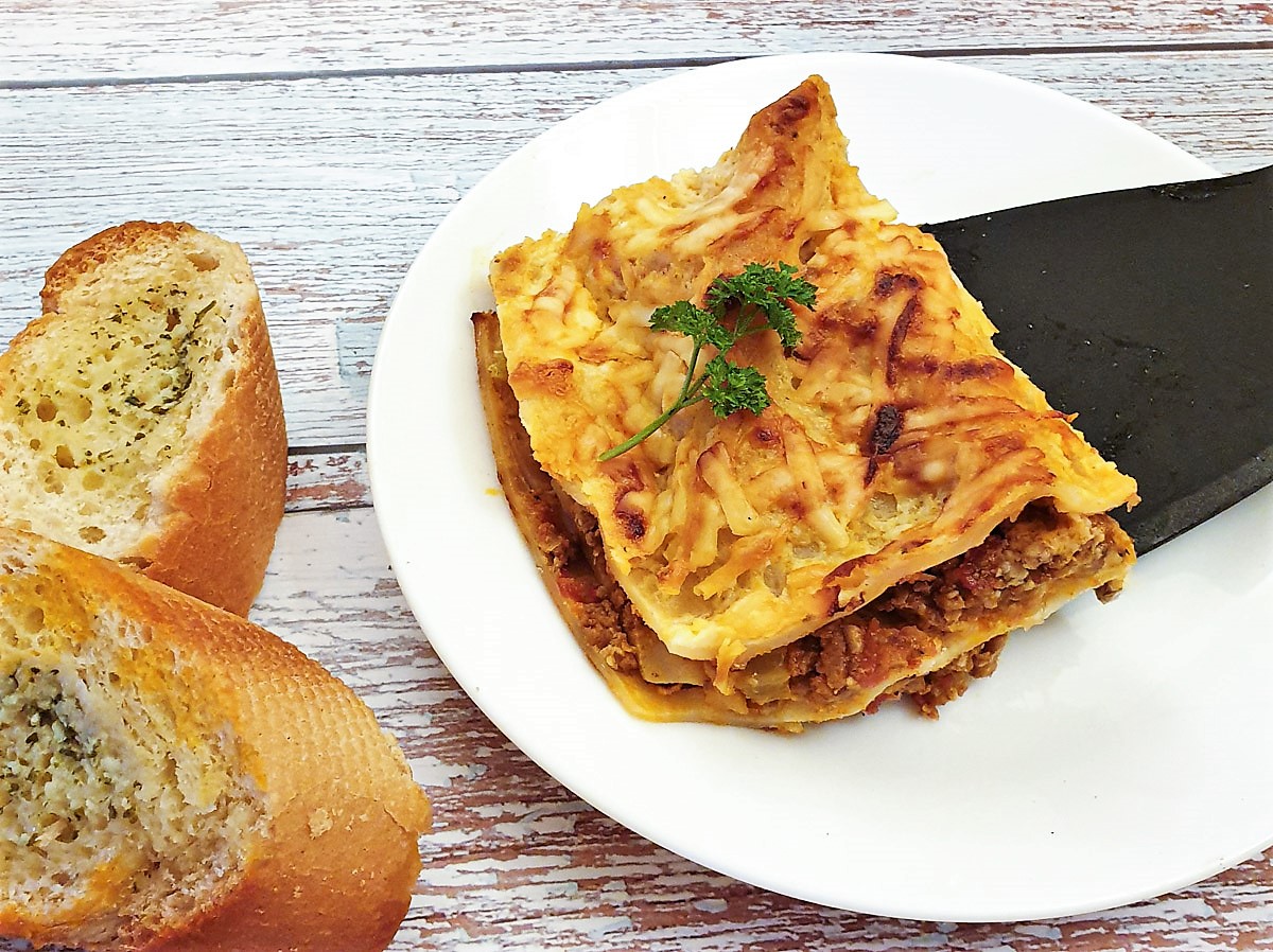 A slice of lasagne being lifted onto a plate with a spatula.