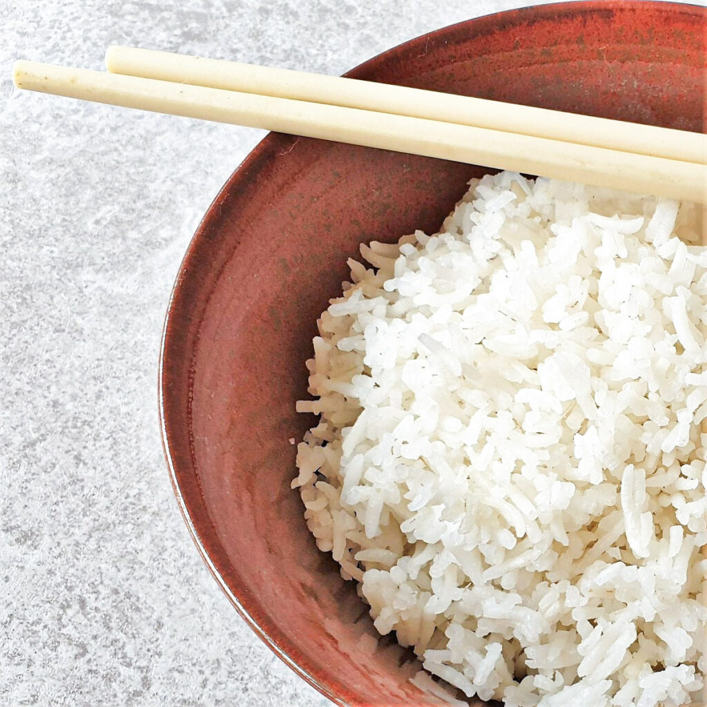 A bowl of white rice with a pair of chopsticks.
