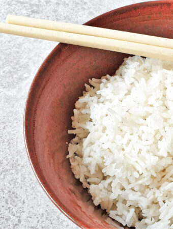 A bowl of white rice with a pair of chopsticks.
