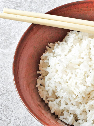 A bowl of white rice with a pair of chopsticks.